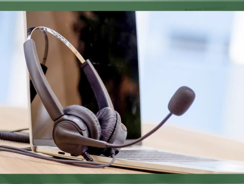 A headset with a microphone sits on top of an open laptop in a call center.